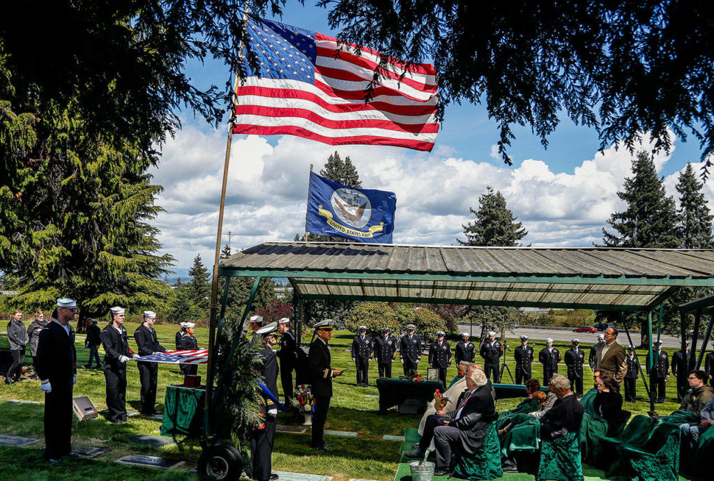 A chaplain from Naval Station Everett, Lt. Jisup Choi, leads the memorial service for Seaman 1st. Class Daniel Guisinger Jr. beneath a covered seating area at Cypress Lawn Memorial Park in Everett on April 27. (Dan Bates / The Herald)
