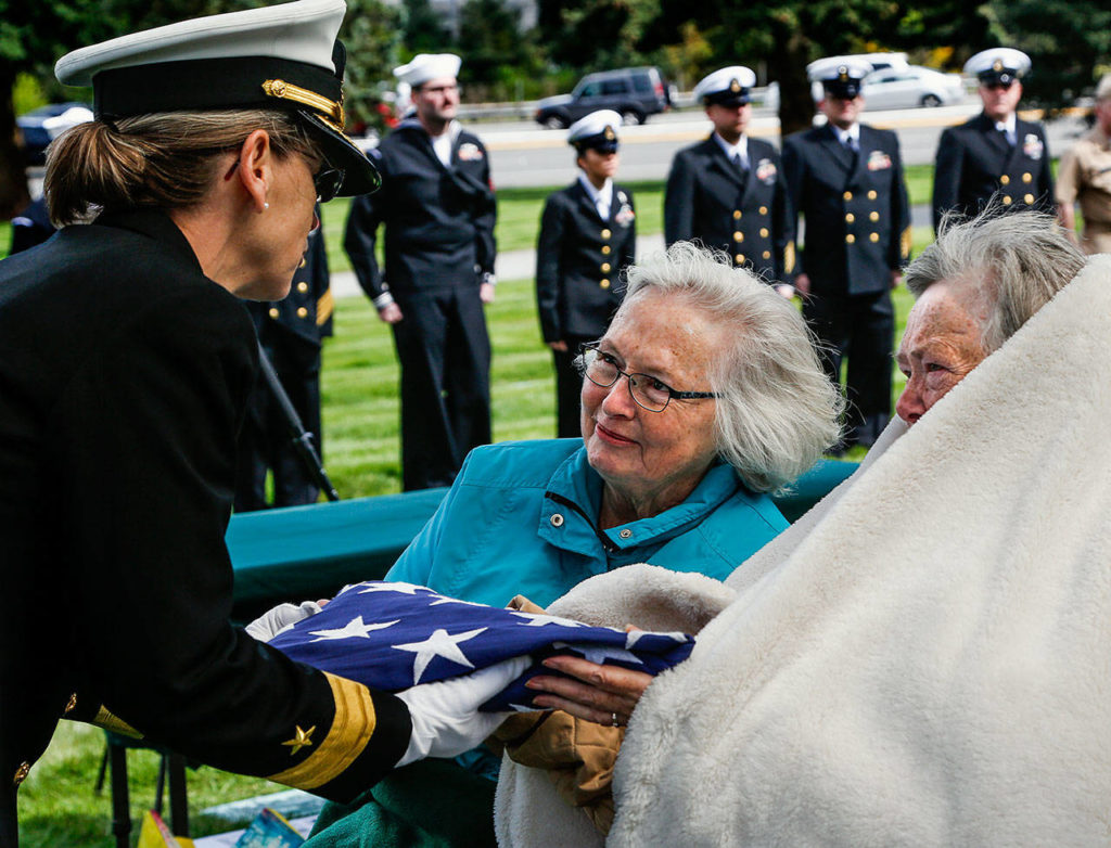 Rear Adm. Linnea Sommer-Weddington, who is with the U.S. Strategic Command in Nebraska, presents a folded American flag to Judy Price and her sister Lana Williams (right). Their mother was the sister of Daniel Guisinger, an Everett sailor who died at Pearl Harbor. (Dan Bates / The Herald)
