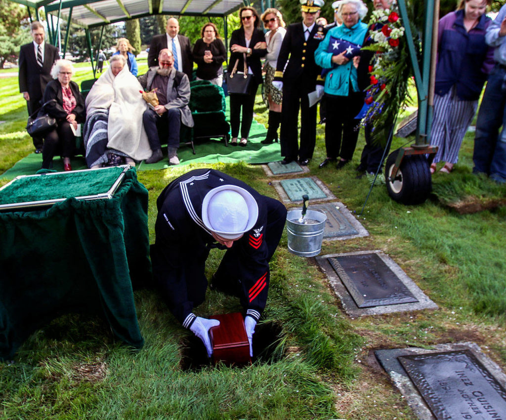 In a somber moment, as family looks on, a sailor places the urn holding Daniel Guisinger’s ashes into his grave. (Dan Bates / The Herald)
