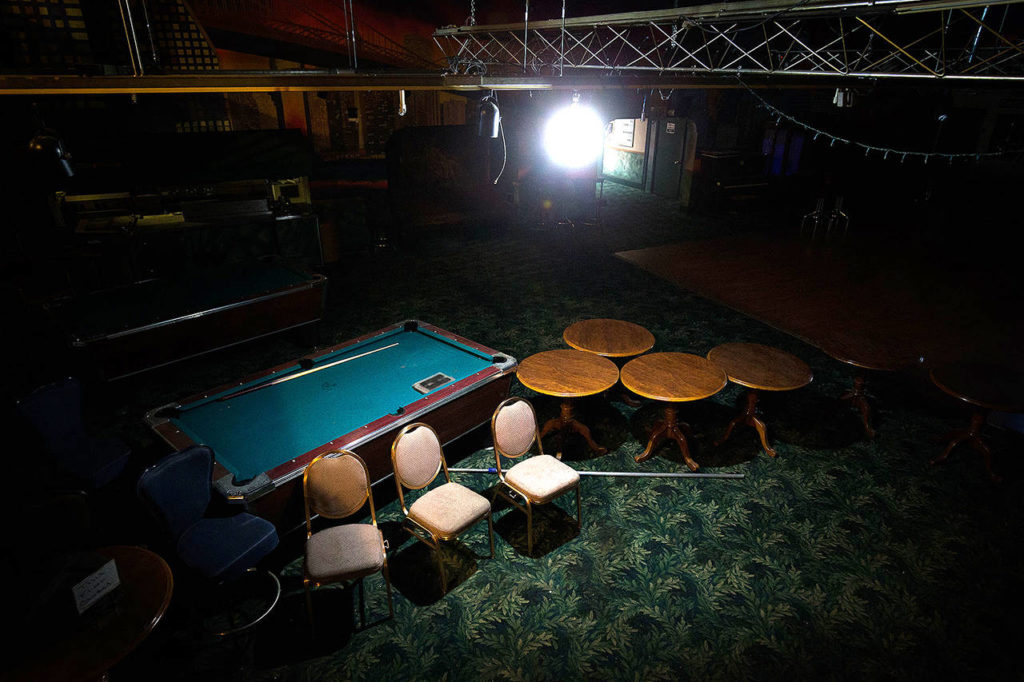 A single light shines on abandoned pool tables, chairs and tables on the first floor inside of Club Broadway on May 1 in Everett. (Andy Bronson / The Herald)
