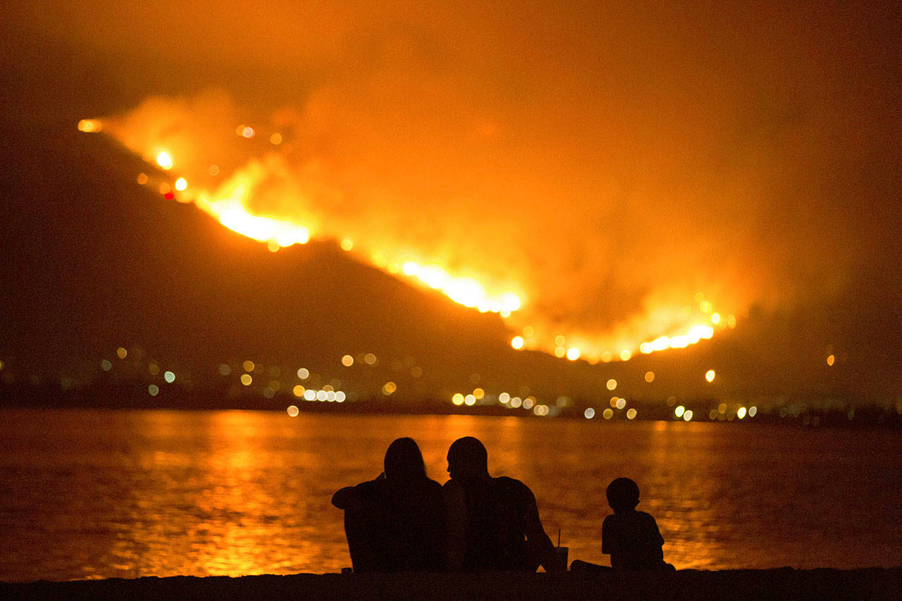 A family sits along the shore of Lake Elsinore as they watch the Holy Fire burn in the distance in Lake Elsinore, California, on Aug. 9. The National Interagency Fire Center is predicting a heavy wildfire season for areas along the west coast of the United States this summer.(AP Photo/Patrick Record, File)