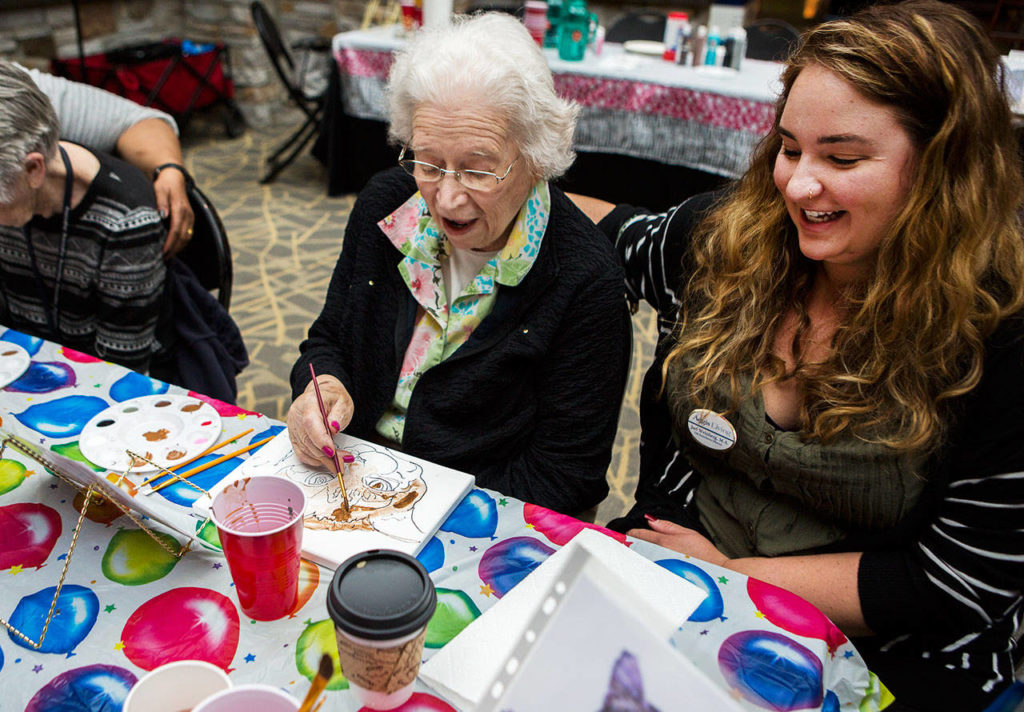 Jael Weinberg (right) laughs with Norma Johnson as Norma paints a cat portrait during Shelter Pet Portraits at the Everett Mall. (Olivia Vanni / The Herald)
