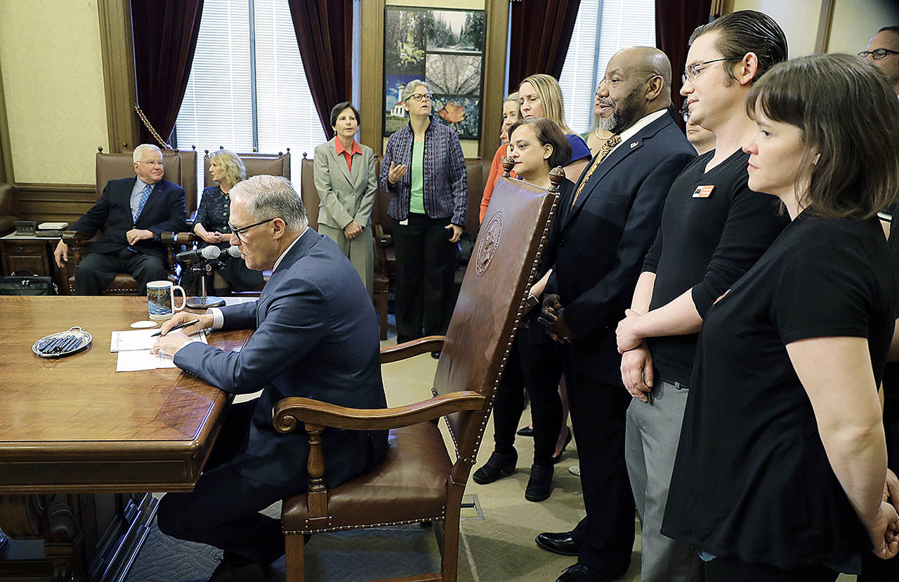 Washington Gov. Jay Inslee signs Senate Bill 5205 into law Tuesday as supporters look on at the Capitol in Olympia. (AP Photo/Ted S. Warren)