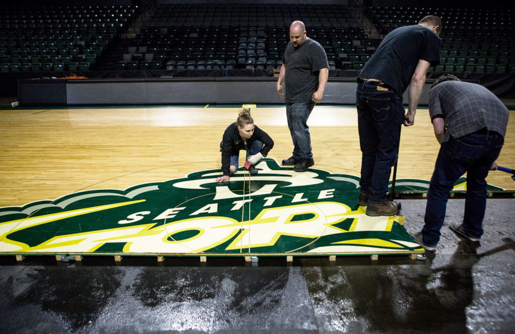 Danielle Pierce (left) and Zach Hendricks (right) check to see if there is any space between the boards during installation of the Seattle Storm’s floor at Angel of the Winds Arena on Monday in Everett. (Olivia Vanni / The Herald)
