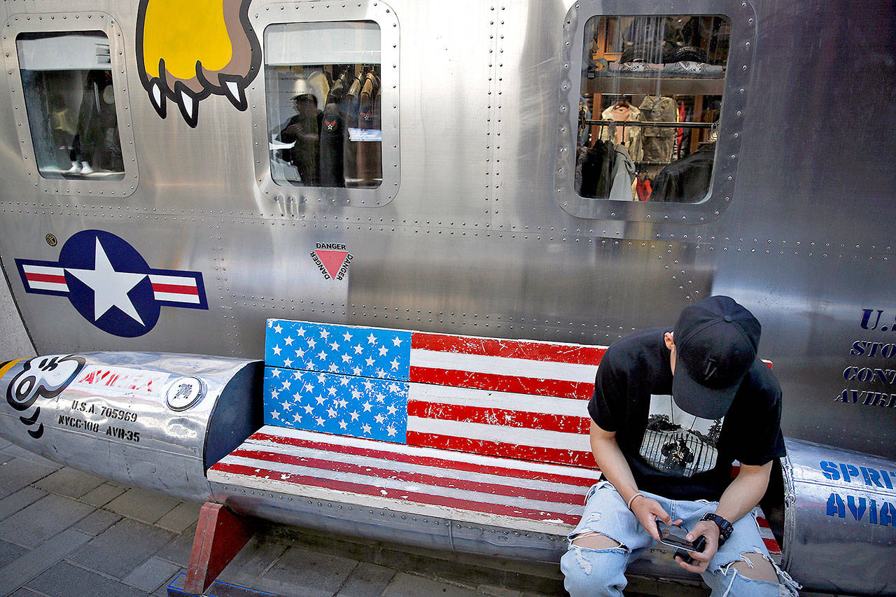 A man browses his smartphone on a bench decorated with a U.S. flag outside a fashion boutique selling U.S.-brand clothing at the capital city’s popular shopping mall in Beijing on Monday. (AP Photo/Andy Wong)