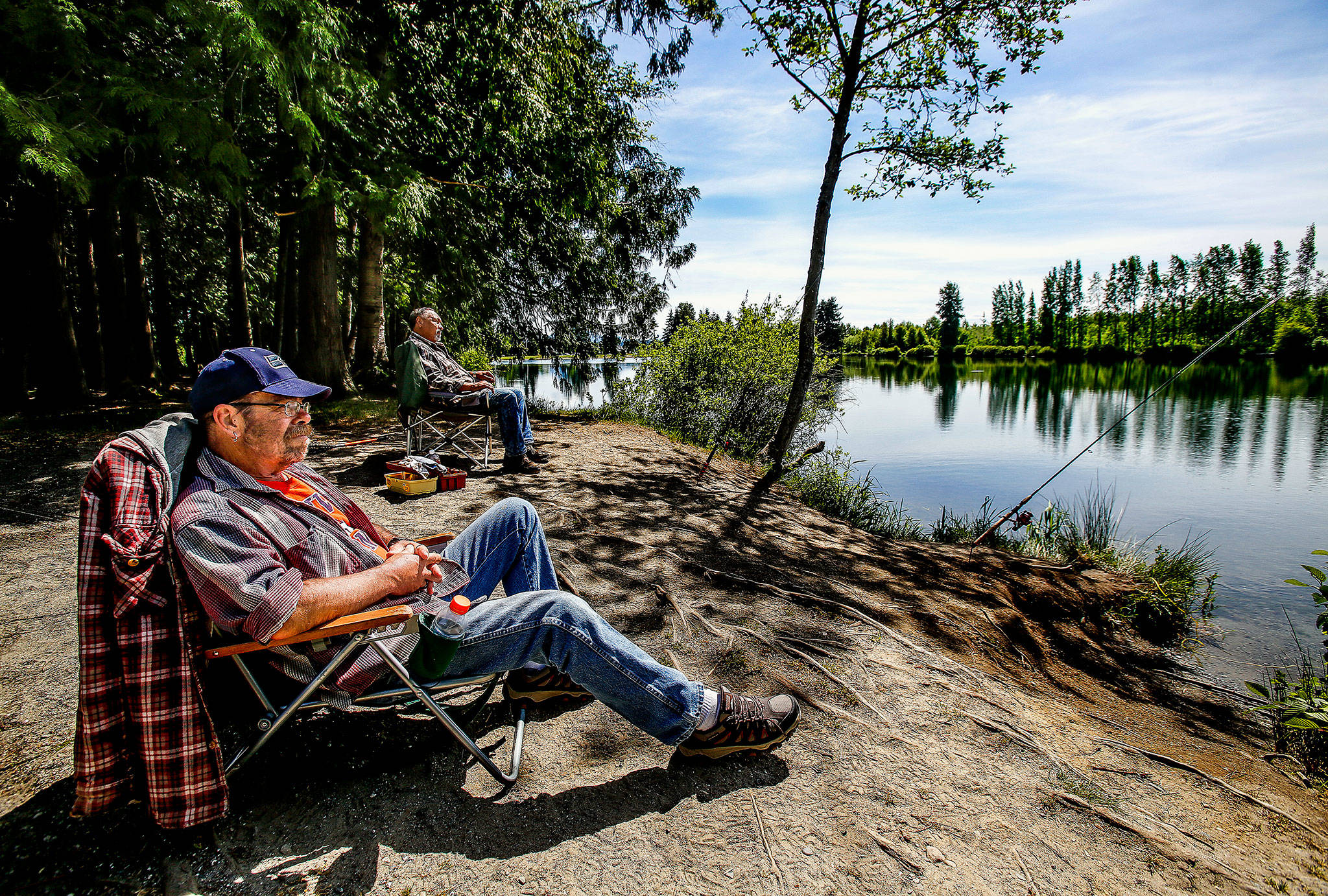 E.J. Silva, 57, foreground, and Clinton Jones, 69, both of Marysville, relax in lawn chairs and enjoy a little fishing Wednesday at the South Lake of Gissberg Twin Lakes county park, which is open year-round to all legal anglers. A $5 parking fee will be required there June 15 through Labor Day. (Dan Bates / The Herald)