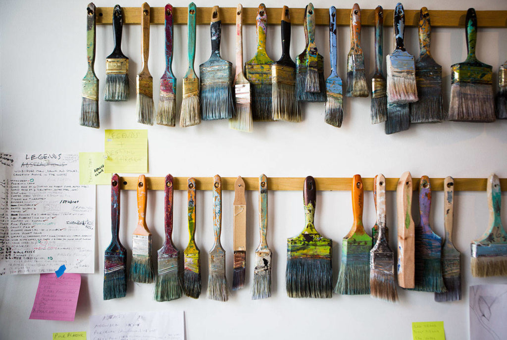 Two racks of paintbrushes and art notes hang on a wall in Knutson’s studio. (Olivia Vanni / The Herald)
