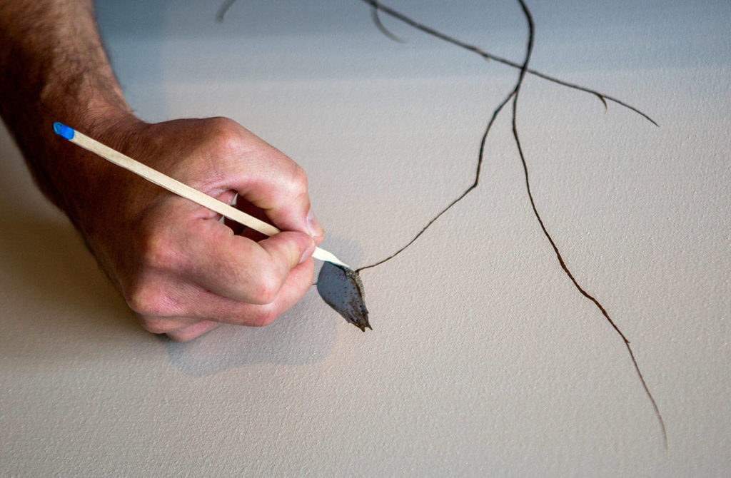 Knutson uses a sharpened coffee stirrer to make a detailed stroke on a painting. (Olivia Vanni / The Herald)
