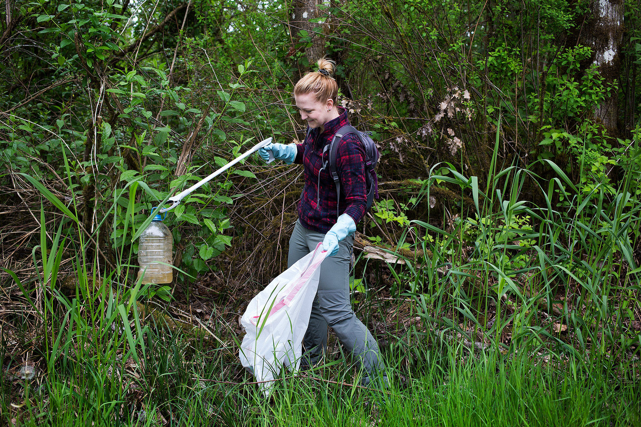 Snohomish’s Sara Thein, founder of Clean Up Washington, snags a plastic jug that had been discarded along the Lowell Riverfront Trail in Everett. (Andy Bronson / The Herald)