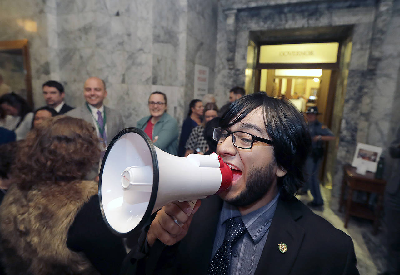 Eduardo Carrillo, of Gov. Jay Inslee’s office, uses a bullhorn to announce upcoming bill signings outside Inslee’s office Tuesday at the Capitol in Olympia. Inslee signed the state’s capital, operating, and transportation budgets, officially designating funds — and new taxes — to pay for state programs for the next two years. (AP Photo/Ted S. Warren)