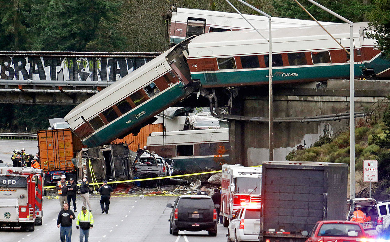 FILE - In this Dec. 18, 2017 file photo, cars from an Amtrak train lie spilled onto Interstate 5 below alongside smashed vehicles as some train cars remain on the tracks in DuPont, Wash. Federal investigators are hearing from witnesses Tuesday, July 10, 2018, as they look into last year’s Amtrak train derailment south of Seattle, Wash., that killed three people and injured dozens. (AP Photo/Elaine Thompson, File)                                In this Dec. 18, 2017 photo, cars from an Amtrak train lie spilled onto I-5 below alongside smashed vehicles as some train cars remain on the tracks in DuPont. (AP Photo/Elaine Thompson, File)