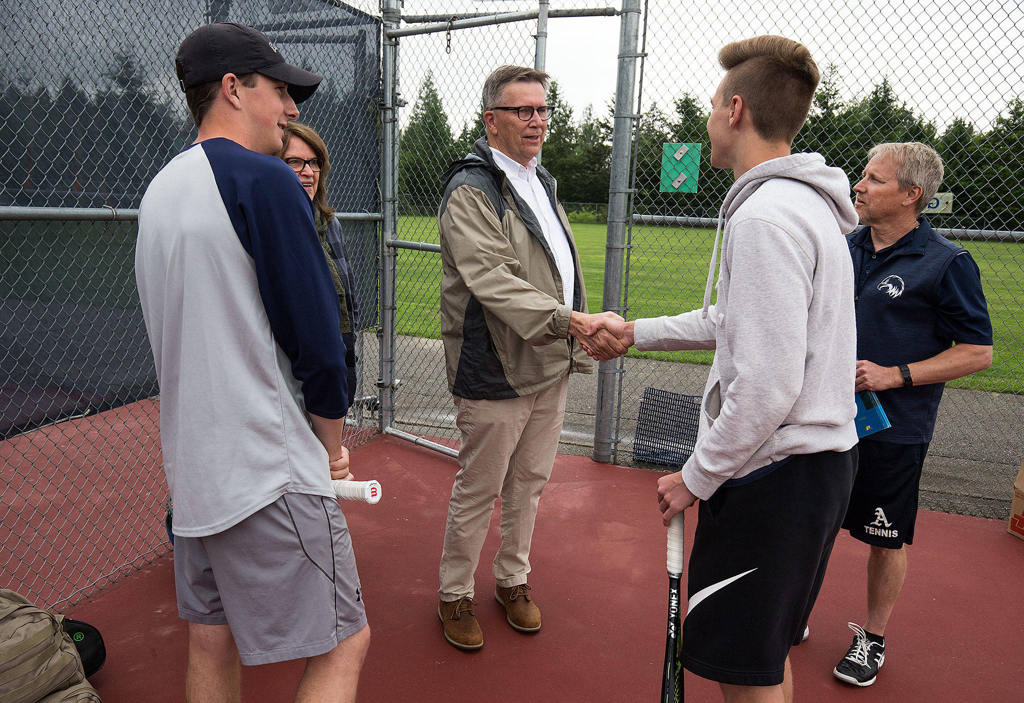 The Arlington doubles team of Ben Spores (left) and Ben Nichols (second from right) meet Doug Grimmius (center), a 1969 Arlington High School graduate and the first Eagles boys tennis player to make state, before practice on May 21 in Arlington. Arlington head coach Ben Mendro is at right. (Andy Bronson / The Herald)