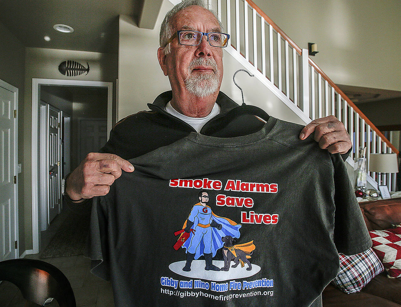 Gerry Gibson holds a T-shirt in 2017 bearing his family’s non-profit company message and logo, with “Gibby” and his dog Nino as the heroes. (Dan Bates / Herald file)