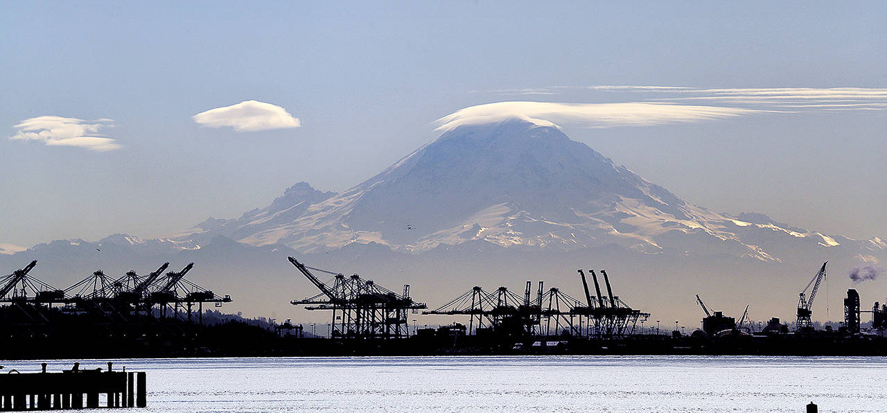 In this 2018 photo, a lenticular cloud forms a cap atop Mount Rainier behind cranes that service container ships in Seattle. From airplanes made by Boeing to apples, cherries and wheat grown by farmers, no other state is more dependent on international trade than Washington. (AP Photo/Elaine Thompson, File)