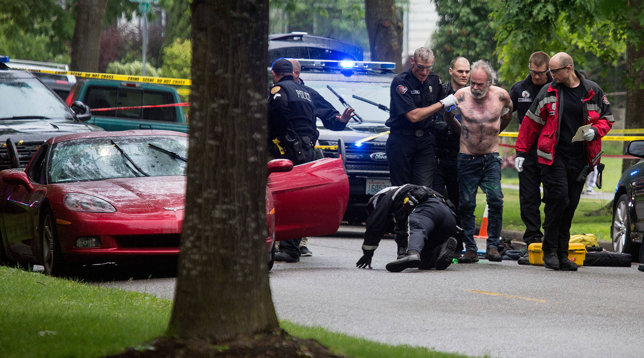 Everett Police examine a Chevy Corvette as medics take a handcuffed man, suspected in a fatal shooting, to an ambulance Friday in Everett. (Andy Bronson / The Herald)