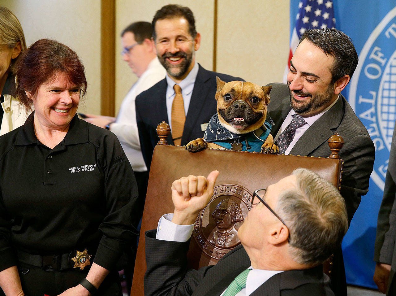 Sen. Guy Palumbo (right), D-Maltby, holds Smudge, a French bulldog, as Gov. Jay Inslee, (seated) looks on before signing a bill in April, 2017, at the Capitol in Olympia, that adopted new penalties for dog owners who tie up or “tether” their dogs in an inhumane way. Palumbo announced his resignation from the Senate last week to take a lobbying job with Amazon. (Ted S. Warren / Associated Press file photo)