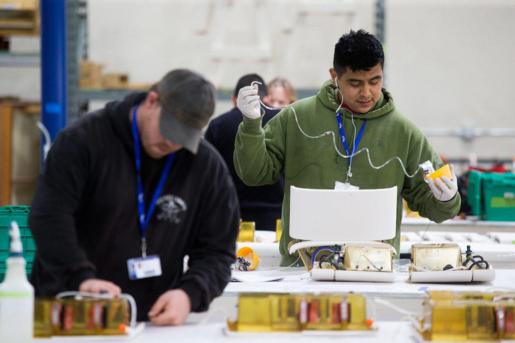 Guillermo Gomez (right) installs a new mask in an oxygen box at Commercial Aircraft Interiors’ new building in Arlington. (Andy Bronson / The Herald) 

