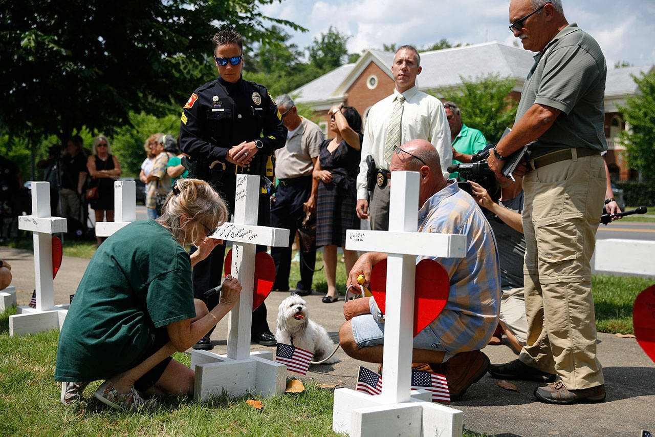 A woman who did not wish to be identified writes a note on the back of a cross for Michelle Langer, a victim of a mass shooting at a municipal building in Virginia Beach, Va., at a nearby makeshift memorial Sunday. (AP Photo/Patrick Semansky)