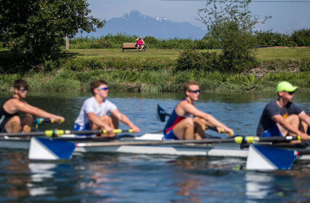 A man watches the Everett Rowing Association’s varsity 8-plus-cox boat team with binoculars during a May 31 practice on the Snohomish River in Everett. (Olivia Vanni / The Herald)
