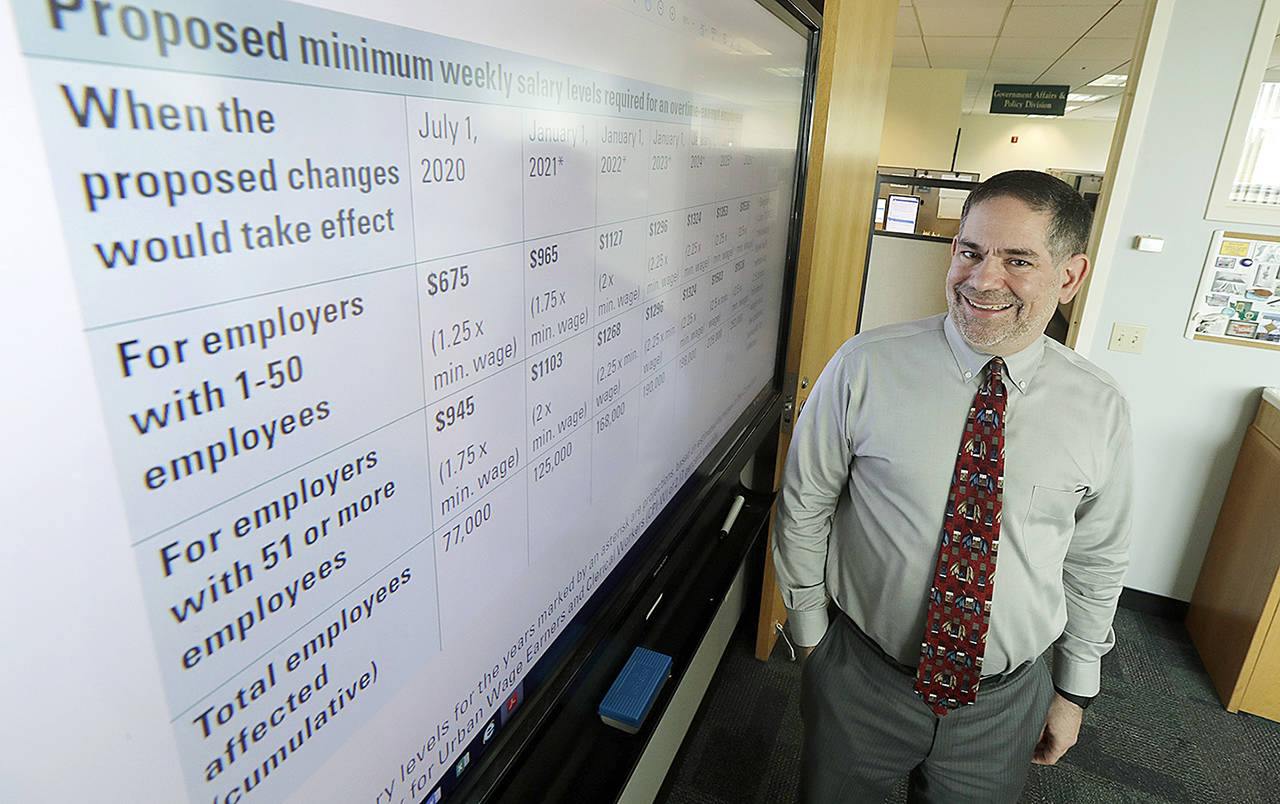 Joel Sacks, director of the Washington state Department of Labor and Industries, poses for a photo Wednesday in his office in Tumwater next to a an information sheet showing how more than 250,000 workers in Washington state would be newly eligible for overtime pay by 2026 under a rule proposed Wednesday by L&I. (AP Photo/Ted S. Warren)