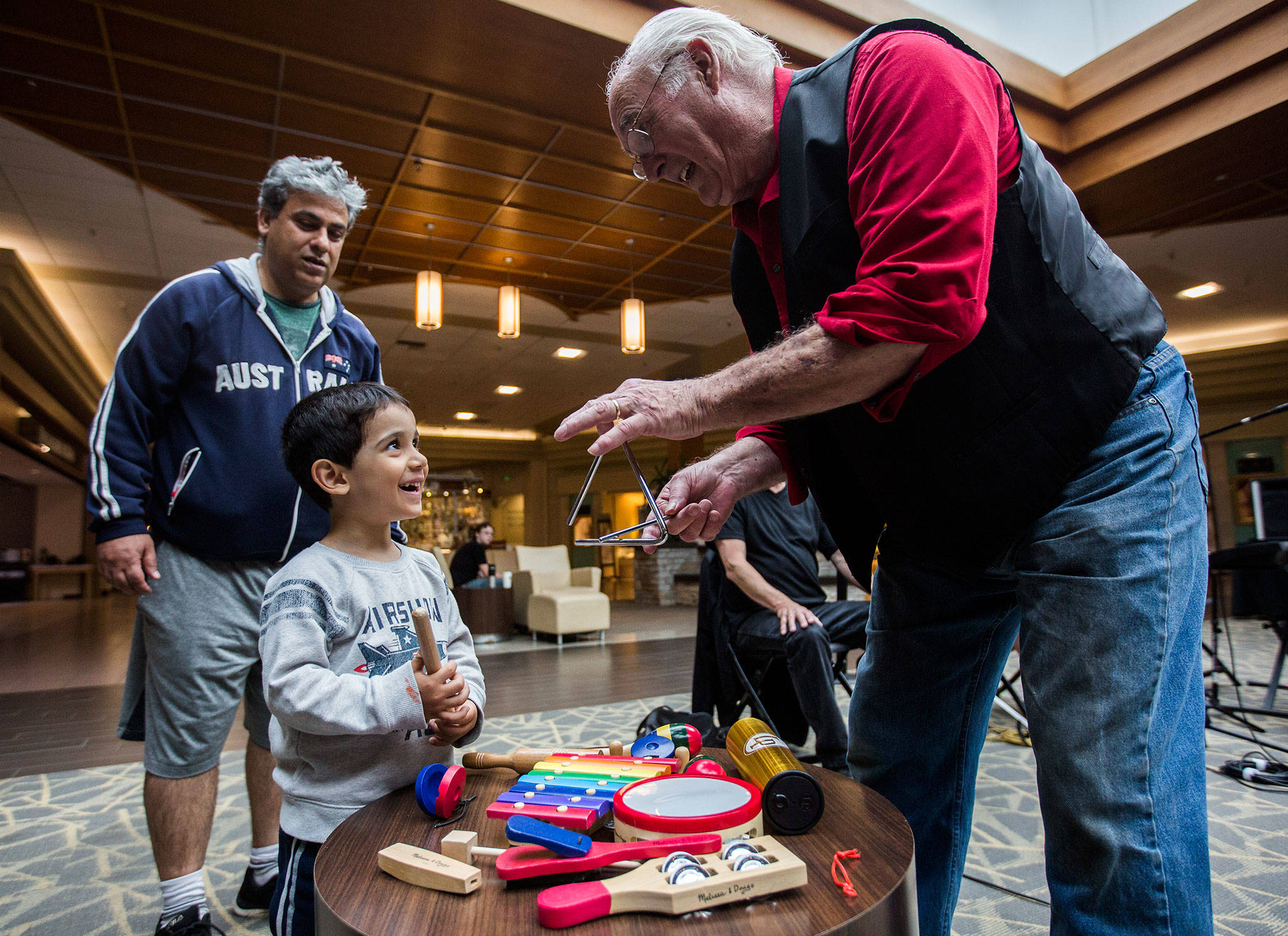 Will Beard shows Ryan Nazari, 3, how to play the triangle during a performance by the Inclusion Jam Project at the Everett Mall. (Olivia Vanni / The Herald)