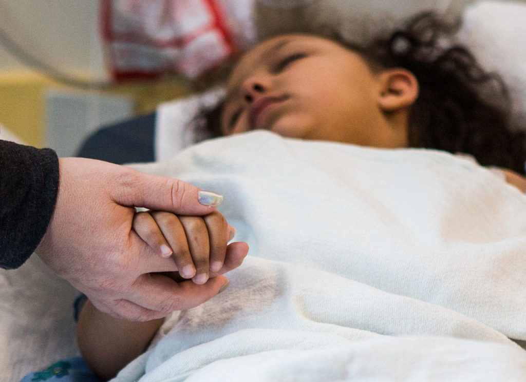 Jasmine holds Kaya’s hand as she starts to wake up from her anesthesia at Seattle Children’s Hospital on Dec. 12, 2018. (Olivia Vanni / The Herald) 
