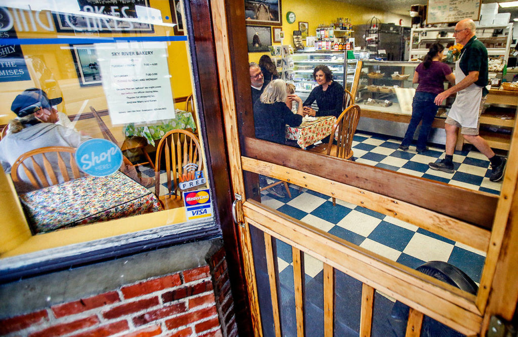 Sky River Bakery co-owner Andrew Abt (white apron) walks over to visit a table full of regulars Tuesday morning. (Dan Bates / The Herald)
