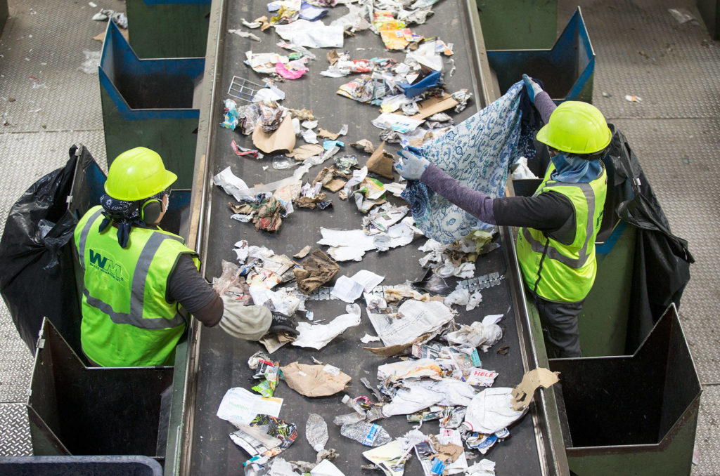 A worker pulls out a dress from recycled waste at Waste Management’s recycling center Aug. 28, 2018 in Woodinville. New rules for what can be accepted as recycling means learning new habits before taking it to the curb. (Andy Bronson / The Herald)
