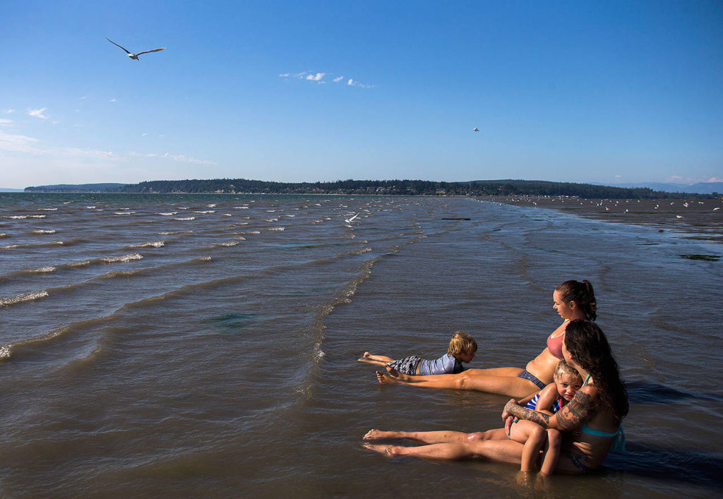 Melissa Simons (right) holds Jet Juliann, 3, while Ashley Allege (center) watches Lincoln Ballard, 3, swim in the water off of Jetty Island on July 5, 2018 in Everett. (Olivia Vanni / Herald file)
