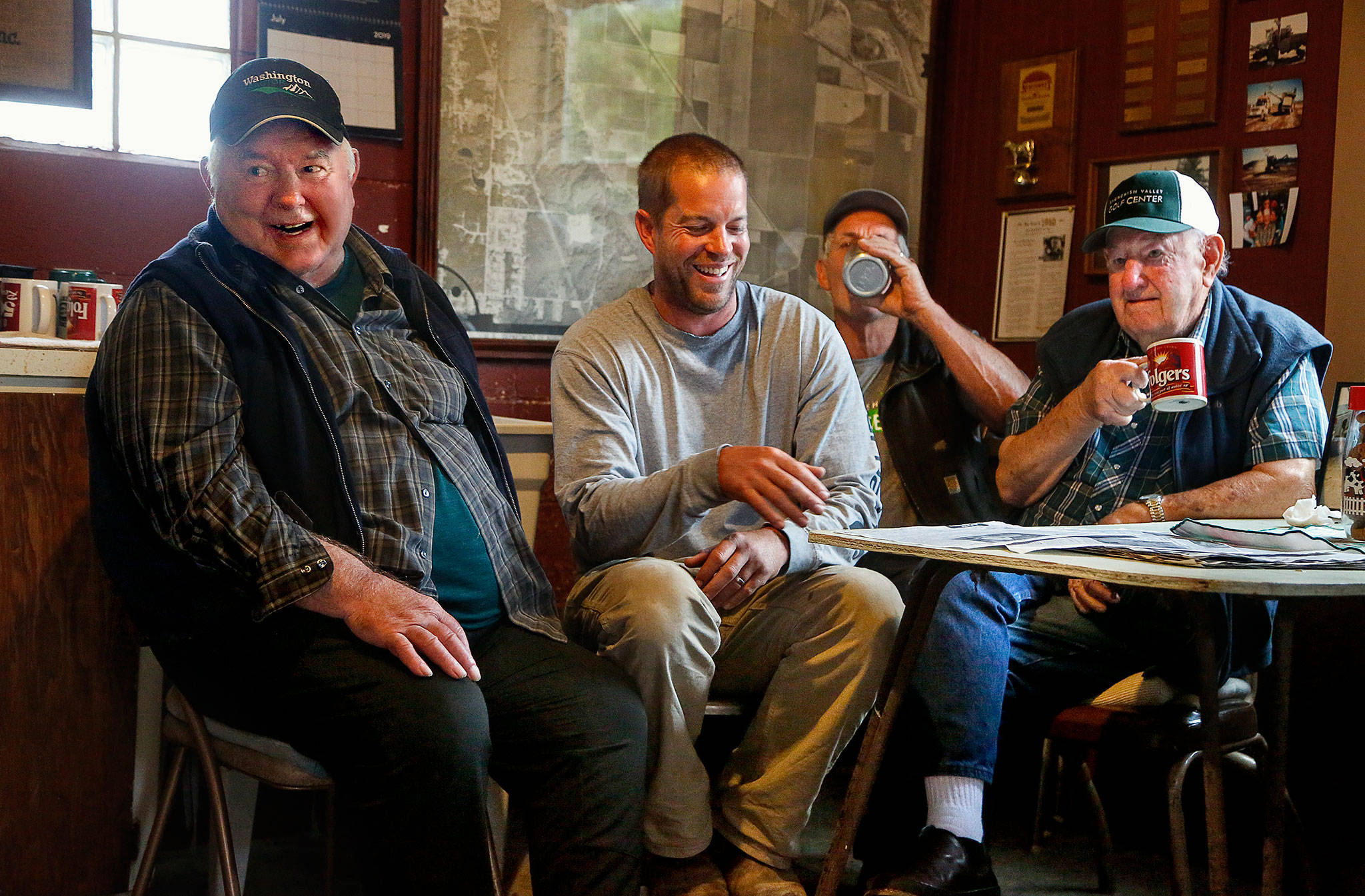 Retired farmers Stub Craven (left) and his brother, Bill (right), enjoy coffee and telling stories, some pretty darned funny, every morning except Sunday at 7 a.m. in their own “coffee shop” in an old milkhouse outside a barn on the Lowell Larimer Road. On Wednesday they were joined by TJ Stocker, 38, middle foreground, and TJ’s dad, Tim Stocker, 61. Tim is Stub’s son-in-law. (Dan Bates / The Herald)