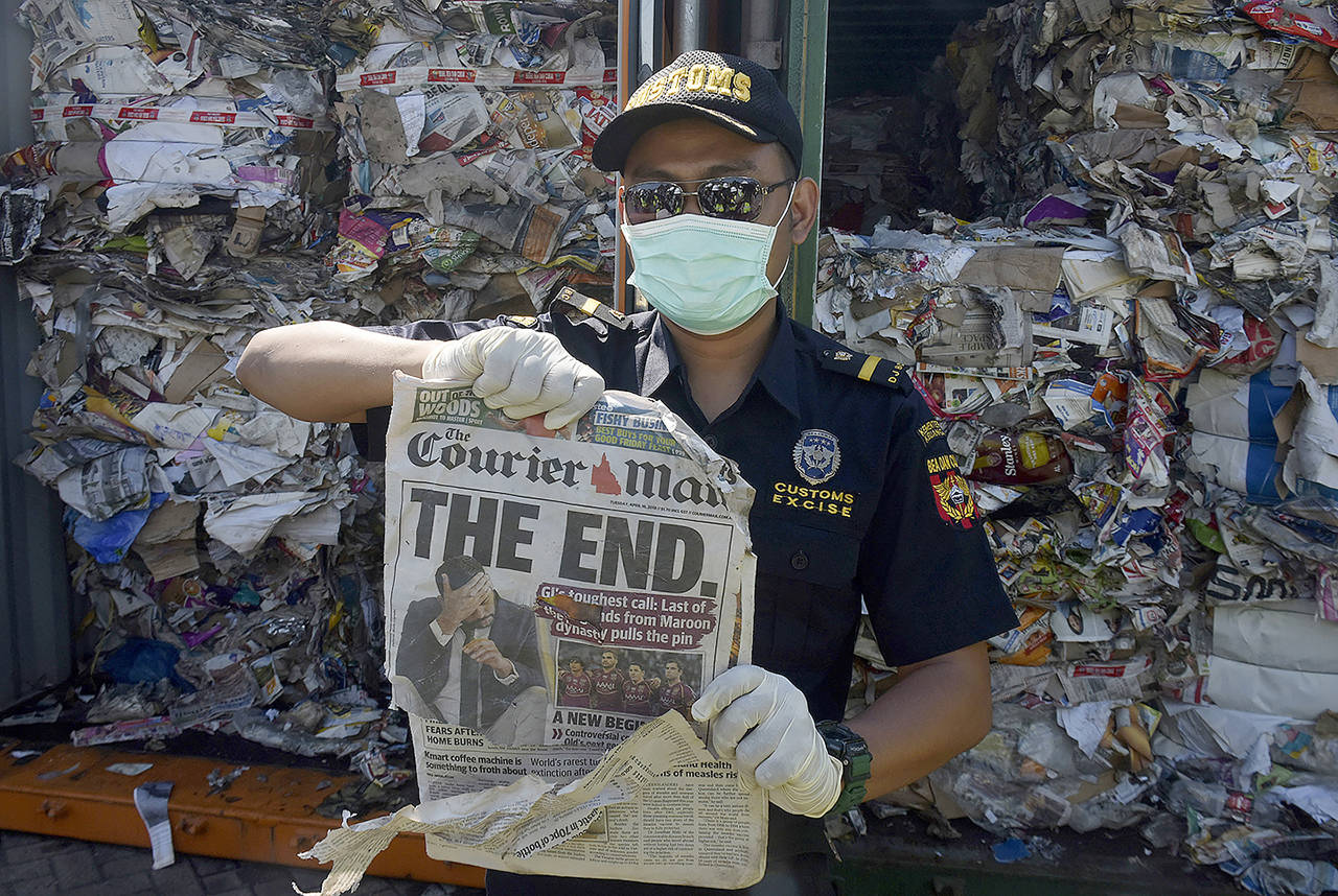 Indonesian custom officers show off the front of a foreign newspaper amoung waste found in a container at the Tanjung Perak port in Surabaya, East Java, Indonesia, on Tuesday. Indonesia is sending dozens of containers of imported waste back to Western nations after finding it was contaminated with used diapers, plastic and other materials. (AP Photo)