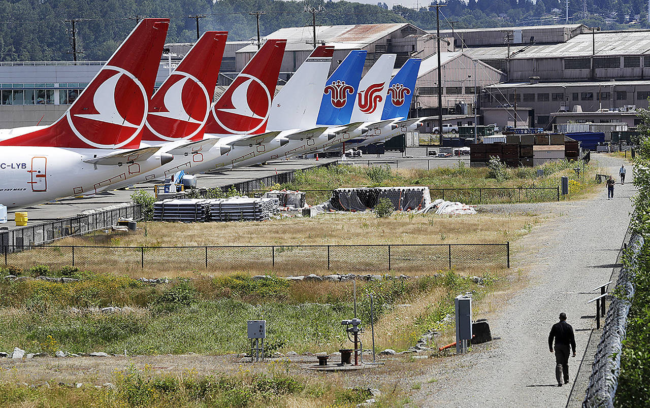 In this June 27 photo, people walk a trail past the tails of several of the dozens of grounded Boeing 737 MAX airplanes lining the edge of a parking area adjacent to Boeing Field in Seattle. (AP Photo/Elaine Thompson, File)