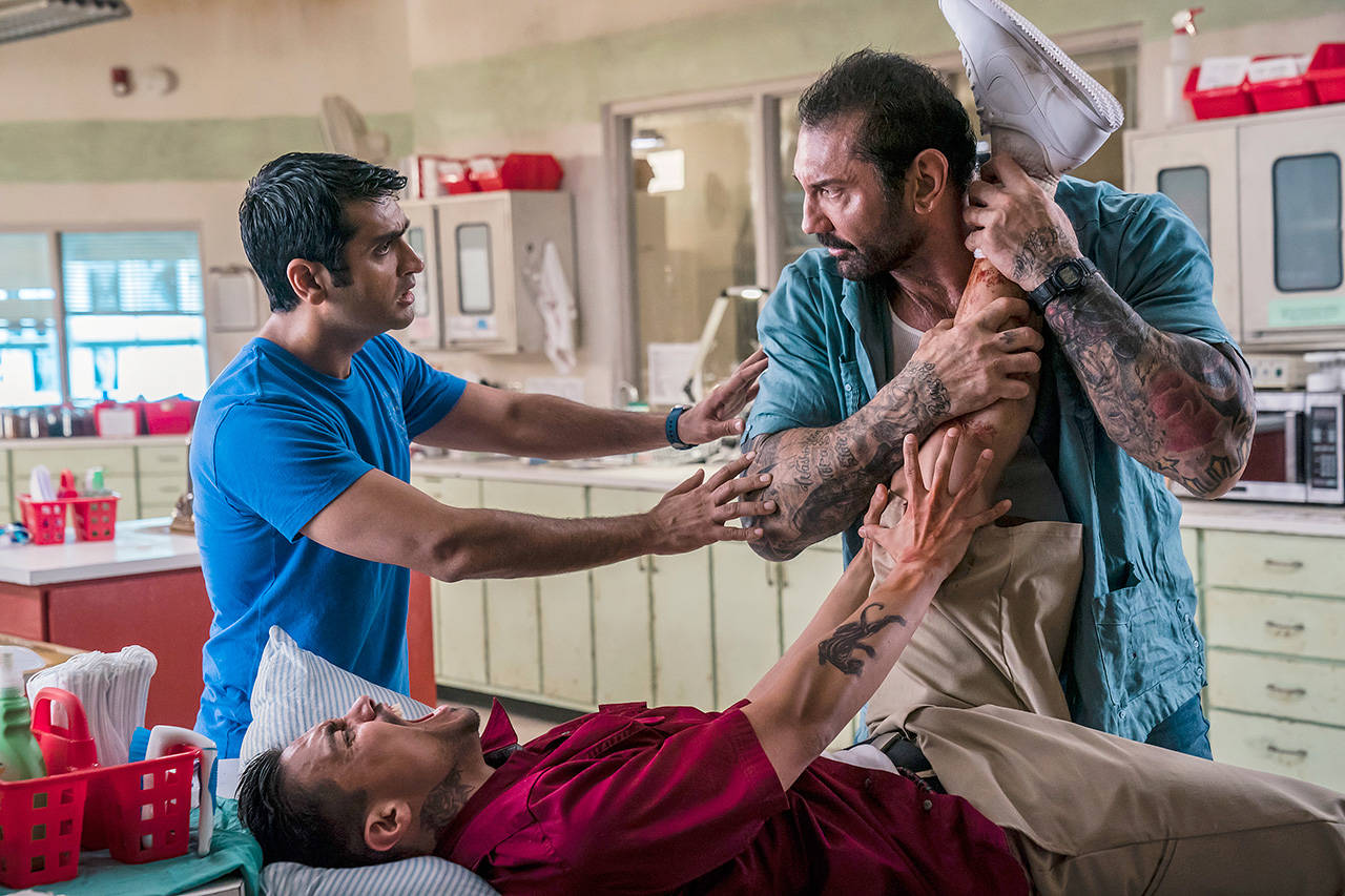 Dave Bautista (right) and Kumail Nanjiani (left, standing) play mismatched buddies in the cop action flick “Stuber.” (20th Century Fox)