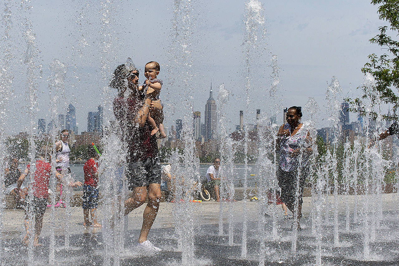 People enjoy the day playing in a water fountain as the Empire State Building is seen from Williamsburg section of Brooklyn on Saturday in New York. Americans from Texas to Maine sweated out a steamy Saturday as a heat wave spurred cancelations of events from festivals to horse races and the nation’s biggest city ordered steps to save power to stave off potential problems. (AP Photo/Eduardo Munoz Alvarez)