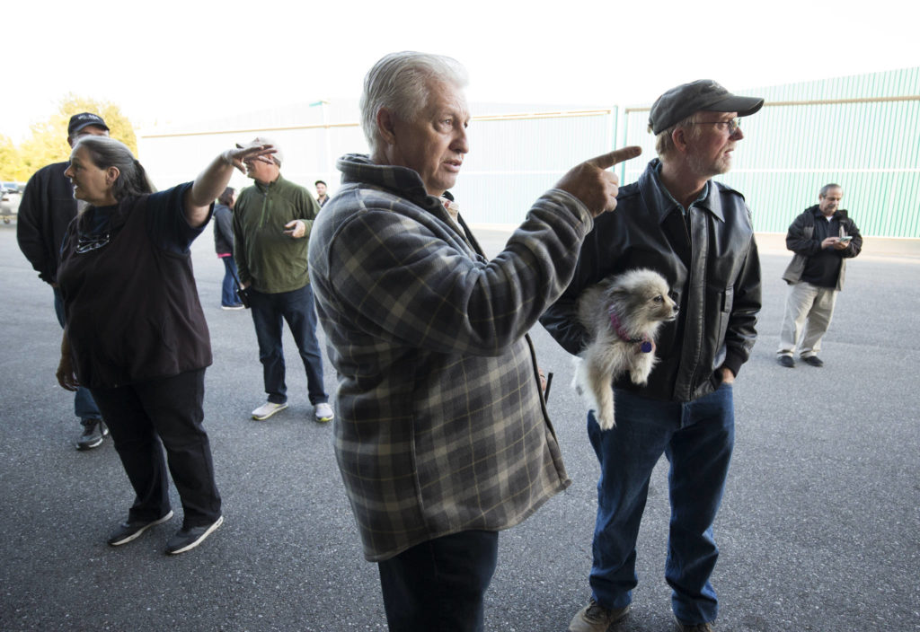 John Norman (center) explains which way pilot Ron Fowler, holding his dog, will take Norman’s replica of the Spirit of St. Louis out for its first flight at Arlington Municipal Airport on July 28. Heather Norman (left) explains the same to a friend. (Andy Bronson / The Herald)
