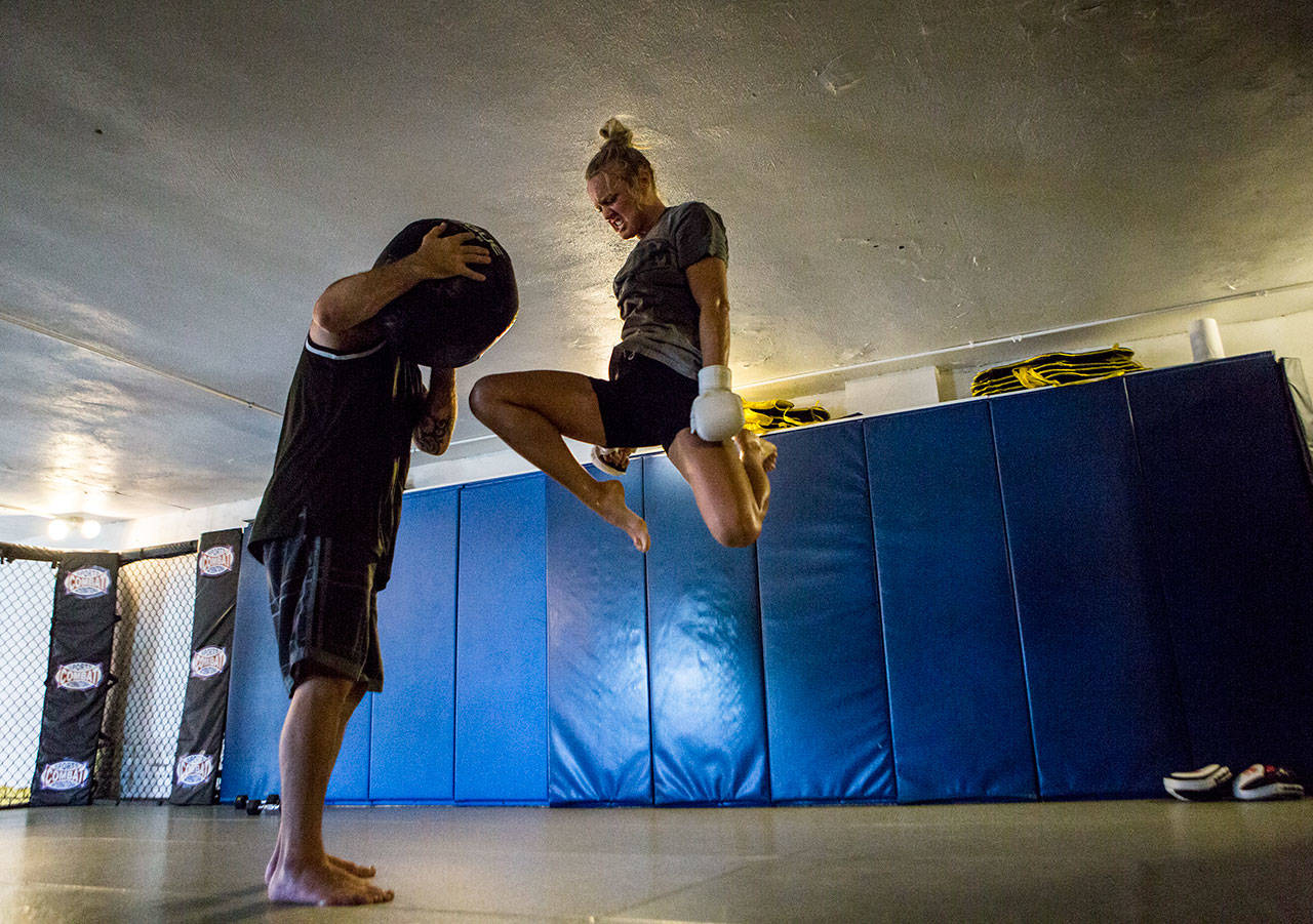 Miranda Granger jumps in the air to knee a medicine ball being held by Charlie Pearson during her training session at Charlie’s Combat Club on July 26, 2019, in Everett. (Olivia Vanni / The Herald)