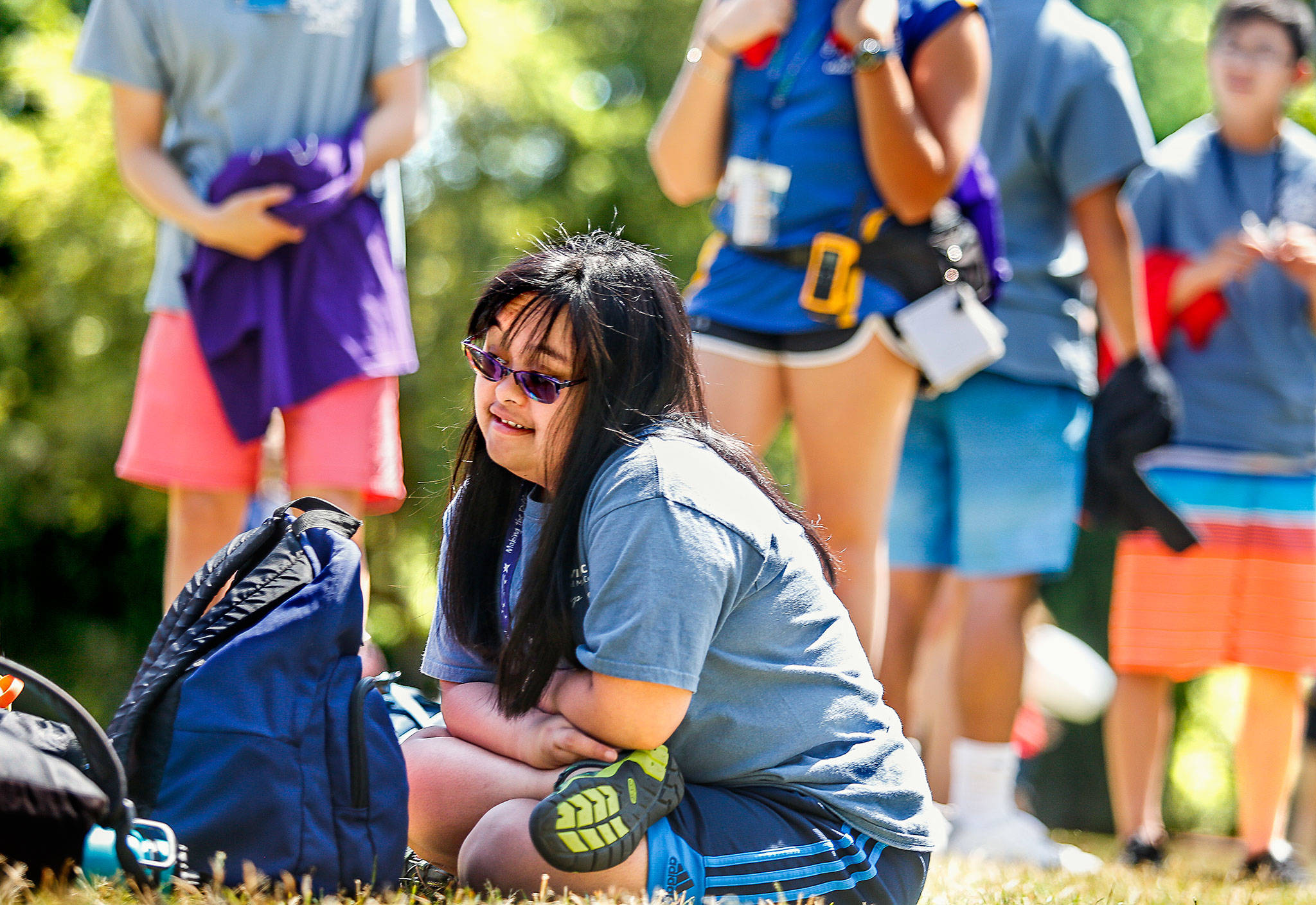 After arriving at Camp Prov in Forest Park on Wednesday, volunteer Bre Baylon sits down on the dry grass and enjoys the sights around her. She’s a former camper in the program for children with special needs. (Dan Bates / The Herald)
