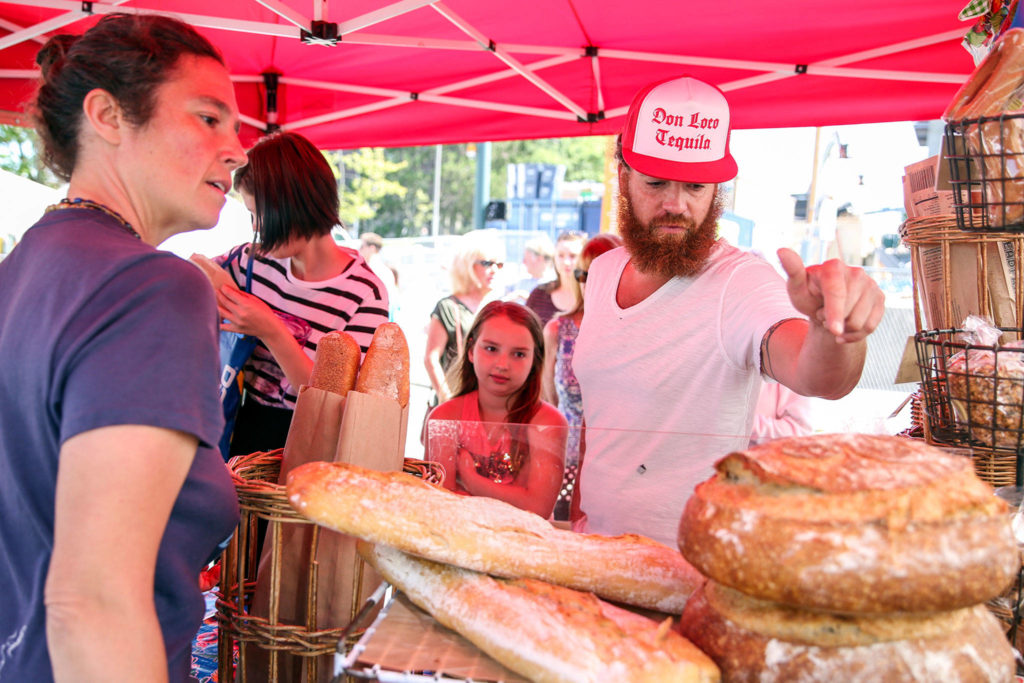 Brotherhood Israel (right) and his daughter Vivid Israel look over the breads of Bread Farm with Ruth Bostwick (left) helping Sunday morning at Everett Farmers Market in Everett. (Kevin Clark / The Herald)
