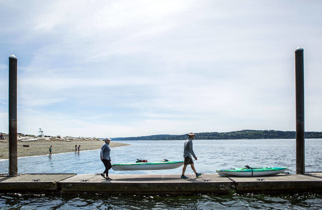 Angela Gonzalez, left, and Juan Gonzalez, right, carry their kayaks out onto the dock at Camano Island State Park. (Olivia Vanni / The Herald)
