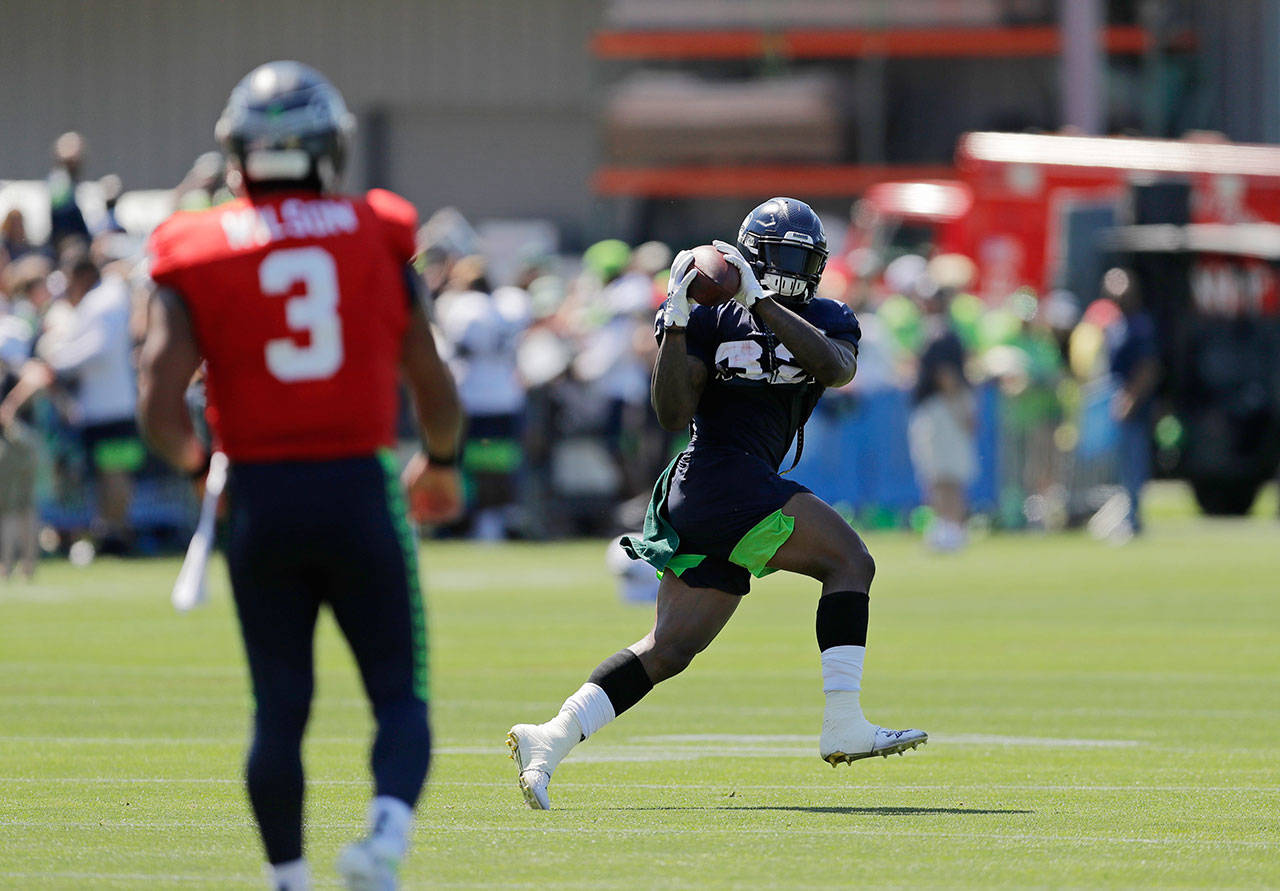 Seahawks running back Chris Carson (right) catches a pass from quarterback Russell Wilson during training camp on July 29, 2019, in Renton. (AP Photo/Ted S. Warren)