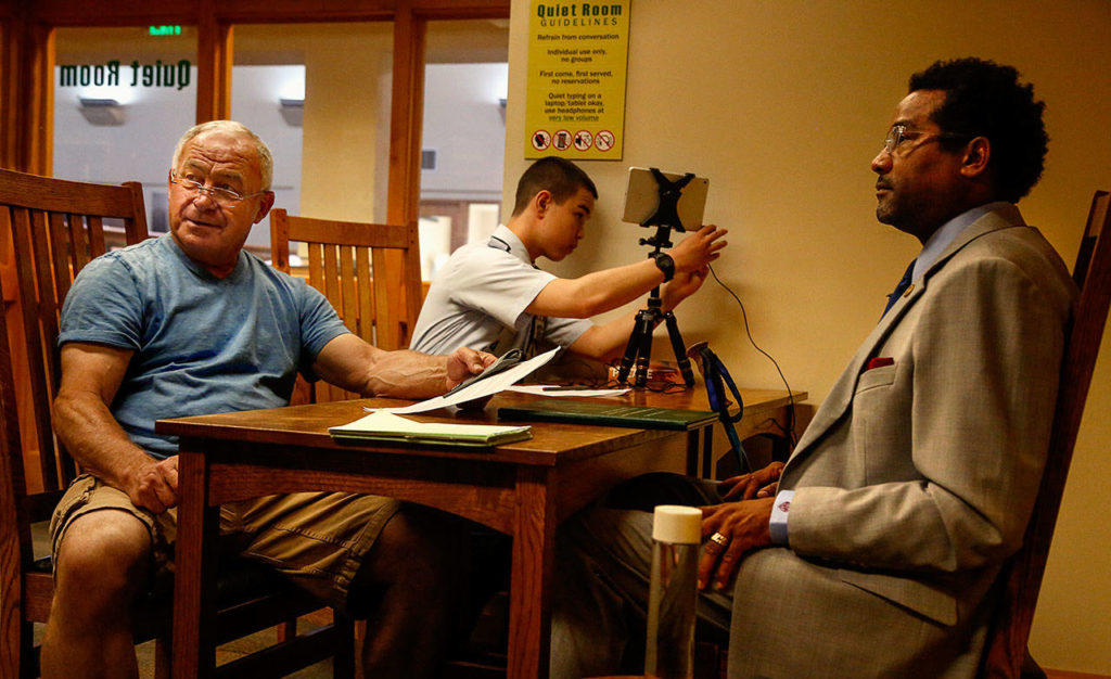 Herbie Martin, (right), who served as a military policeman with the U.S. Army, and 72-year-old Paul Miller, who interviewed Martin, finish up Monday, as John Weir (center) takes down the recording equipment. (Dan Bates / The Herald)
