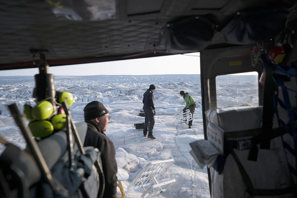 In this Aug. 16 photo, New York University air and ocean scientist David Holland (left) and field safety officer Brian Rougeux (right) are helped by pilot Martin Norregaard as they carry antennas out of a helicopter to be installed at the Helheim glacier, in Greenland. Holland and his NYU team are tracking what’s happening in Greenland from both above and below. (AP Photo/Felipe Dana)
