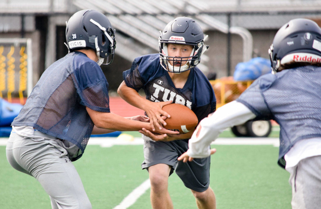 Sultan senior quarterback Willy Bennett hands the ball off to senior running back Aidan Fleming during practice on Aug. 23, 2019, at Sultan High School. (Katie Webber / The Herald)
