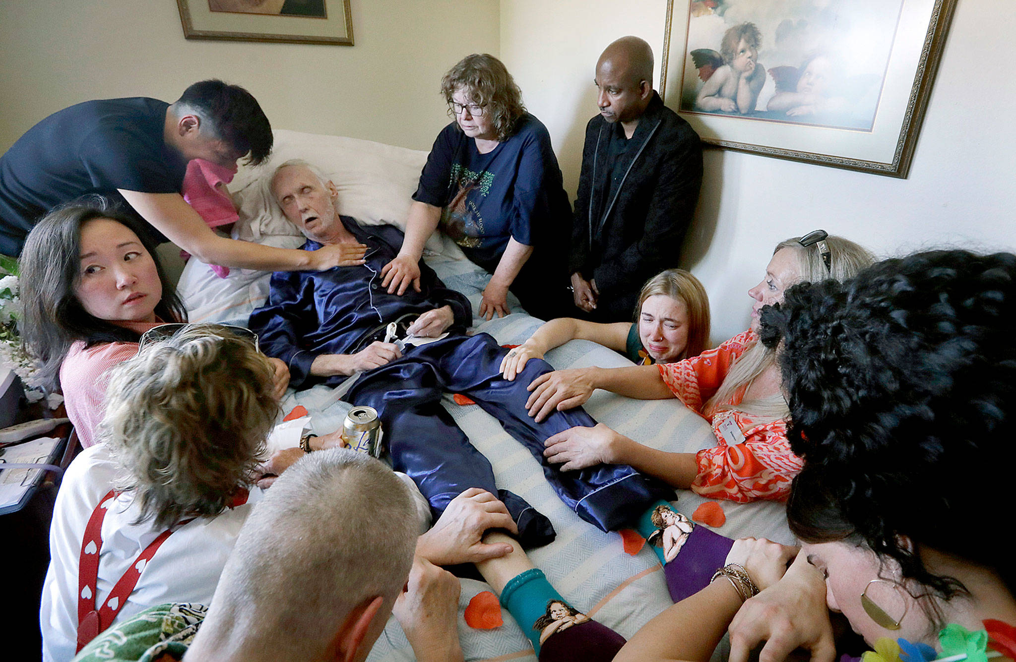 On May 10, Robert Fuller lies unconscious after plunging prescribed drugs to end his life into his feeding tube as his husband, Reese Baxter (upper left), and friends lay hands on him in Seattle. Earlier in the day, Fuller had the party of a lifetime. He’s one of about 1,200 people who have used Washington’s Death with Dignity Act to end their lives in the decade since it became law. (AP Photo/Elaine Thompson)