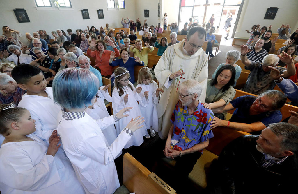 Robert Fuller (seated center right) receives a blessing and prayer from Rev. Quentin Dupont on May 5, among white-robed children who had just received their first communion and the congregation at St. Therese Parish Catholic church in Seattle. (AP Photo/Elaine Thompson)
