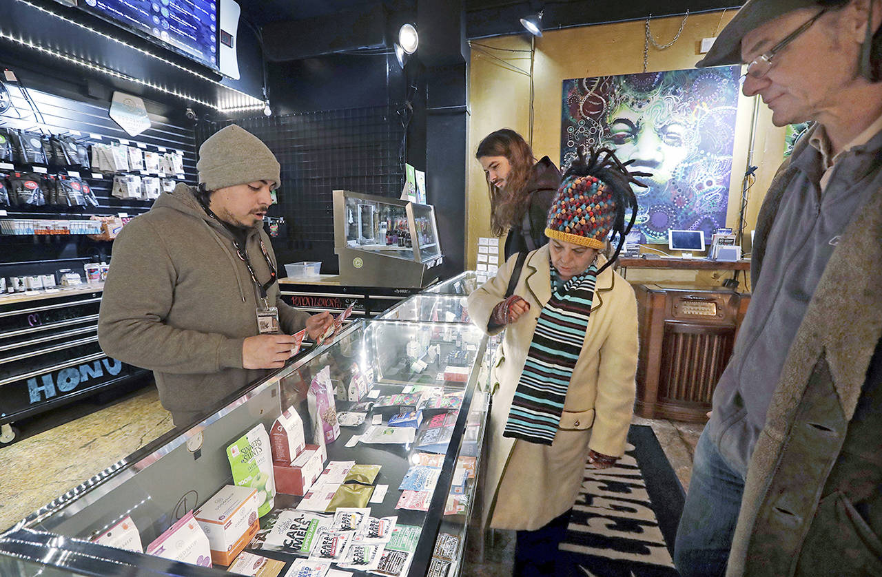 In this 2018 photo, cannabis consultant Juan Aguilar (left) assists customers Bill (right) and Nize Nylen and their son Russell as they shop for edible marijuana products in the Herban Legends pot shop in Seattle. (AP Photo/Elaine Thompson, File)