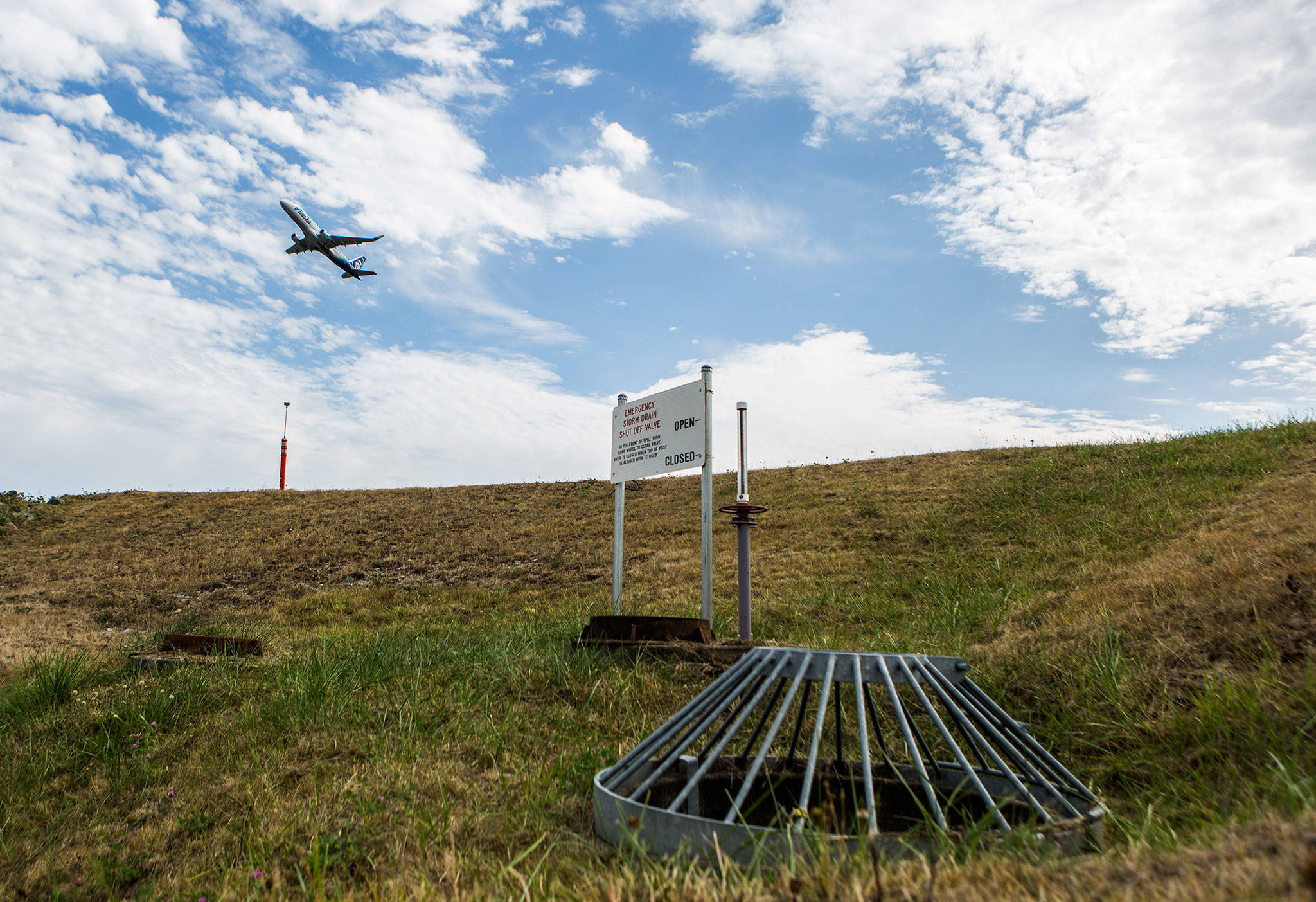 An airplane takes off from the runway over the top of one of the water drainage shut-off valves installed around Paine Field to help prevent water runoff contamination on Sept. 5 in Everett. (Olivia Vanni / The Herald)