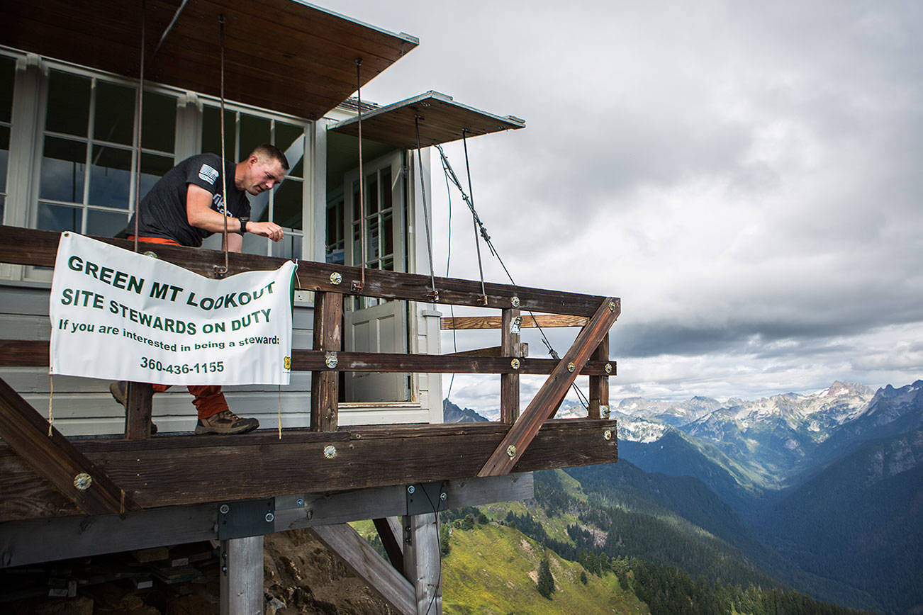 Don Sarver hangs up a Green Mountain Lookout steward interest banner on the outside of the look out on Saturday, Aug. 31, 2019 in Darrington, Wash. (Olivia Vanni / The Herald)