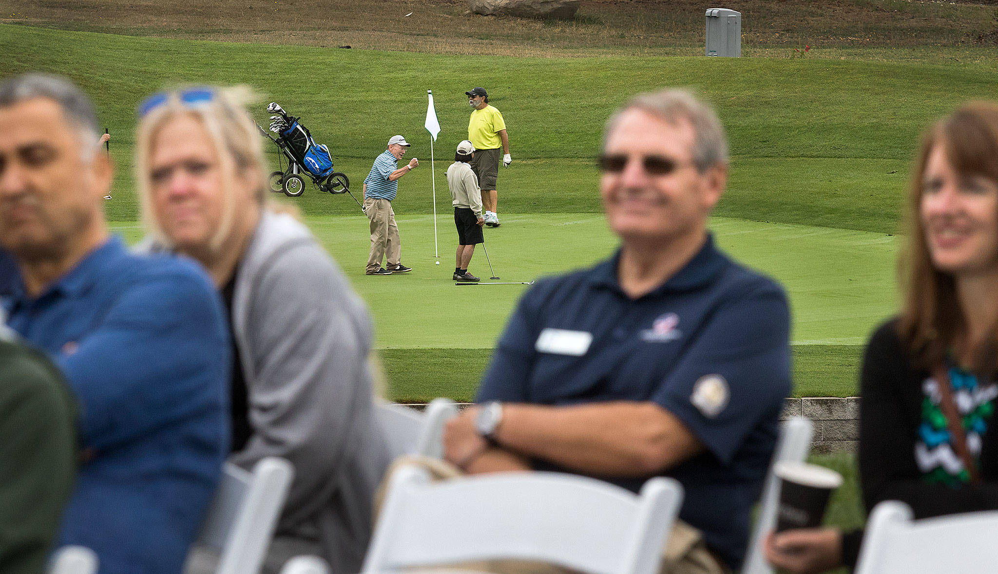 As guests attend a dedication ceremony, a golfer pumps his fist while putting on the newly rebuilt 13th hole at Legion Memorial Golf Course on Wednesday in Everett. The dedication took place near the 14th hole’s tee box to celebrate the renovation project. (Andy Bronson / The Herald)