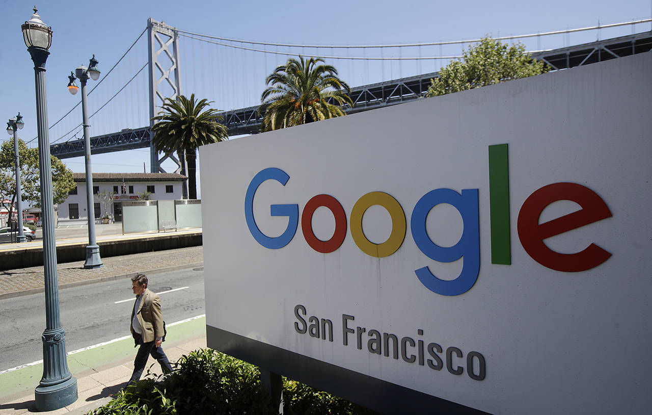 A man walks past a Google sign outside with a span of the Bay Bridge at rear in San Francisco. (AP Photo/Jeff Chiu, File)